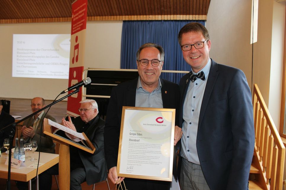 Der Vorsitzende des Kreis-Chorverbandes Bernkastel-Wittlich, Marcus Heintel (rechts), überreicht Landrat Gregor Eibes (links) den Ehrenbrief als Dank für die Zusammenarbeit.