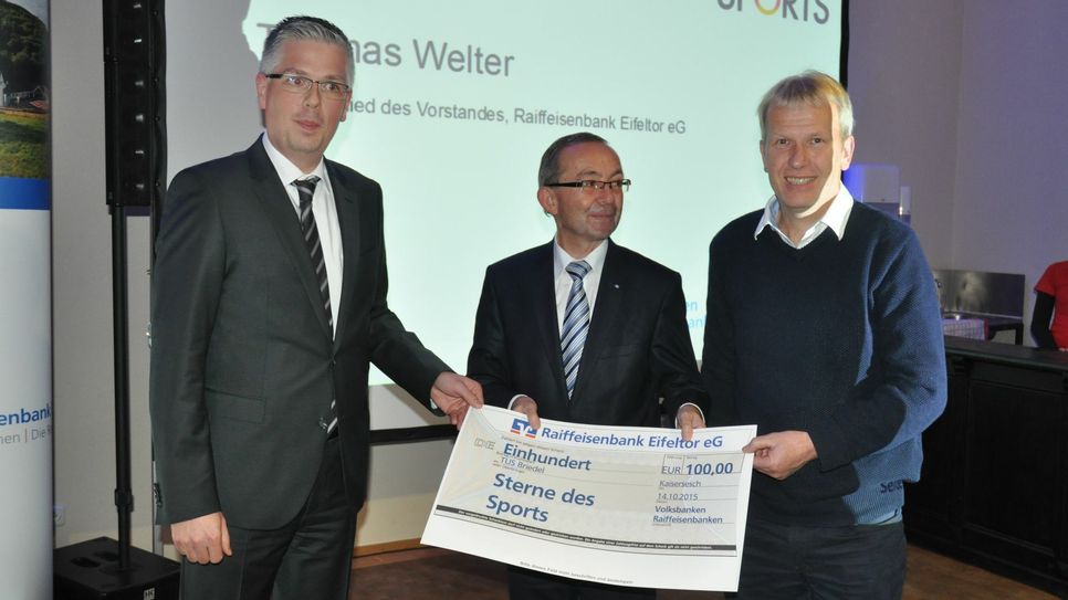 Thomas Welter (Raiffeisenbank Eifeltor) und Walter Hoff (Raiffeisenbank Zellerland) überreichen den Teilnehmerpreis an einen Vertreter des TuS Briedel.