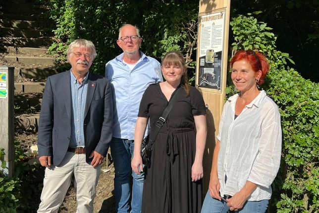 Klaus Onasch (stellvertretender Bürgermeister), die Initiatoren Ben Magrean und Katharina Isabel Franke sowie Ulrike Meissner von der Schreinerei Holzart präsentieren die Holztafel, die auf den Stolperstein an der Dreilägerbachtalsperre in Roetgen hinweist.